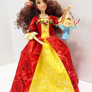 May include: A doll in a red rose-patterned gown with a yellow panel, a floral headpiece, and a small doll. The doll's dress has long sleeves and is trimmed with lace and floral accents. The doll is holding a small doll with a blue dress.