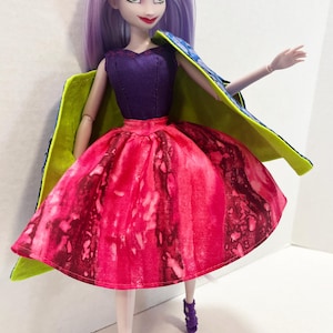 Pu&ograve; includere: Una bambola con lunghi capelli color lavanda, occhi verdi e labbra rosse. La bambola indossa un corpetto senza maniche viola scuro, una gonna con motivo ad acquerello rosa e rosso vivace e un mantello blu con fodera verde lime. Sandali viola.