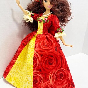 May include: A doll wearing a red gown with a rose pattern, a yellow panel, and a floral crown. The doll has brown curly hair, a pearl necklace, and lace accents on the sleeves. The dress features a full skirt.