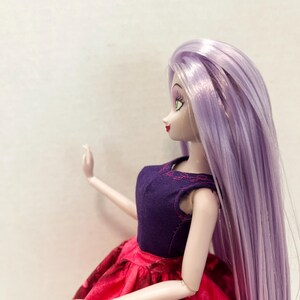 Pu&ograve; includere: Una bambola con lunghi capelli lisci color viola chiaro, che indossa un corpetto senza maniche viola scuro con delicati dettagli a foglia ricamati in rosa sullo scollo, abbinato a una gonna rosso vivace con un sottile motivo floreale scuro.
