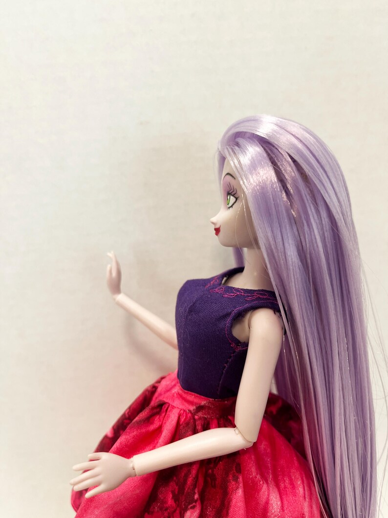 Pu&ograve; includere: Una bambola con lunghi capelli lisci color viola chiaro, che indossa un corpetto senza maniche viola scuro con delicati dettagli a foglia ricamati in rosa sullo scollo, abbinato a una gonna rosso vivace con un sottile motivo floreale scuro.