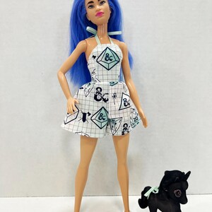 May include: A doll with long blue hair wearing a white halter-style romper featuring a black grid pattern and various gaming dice icons. The doll has light skin, pink lips, and white shoes. Beside the doll stands a small black toy horse figure.