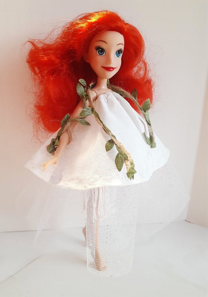 Puede incluir: Una mu&ntilde;eca de pelo rojo con un vestido blanco con un detalle de vid verde y una falda de tul blanca.