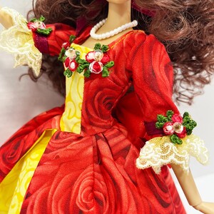 May include: A doll wearing a red dress with a rose pattern. The dress has yellow accents and is adorned with floral embellishments. The doll has brown hair and a pearl necklace. The sleeves have lace cuffs.