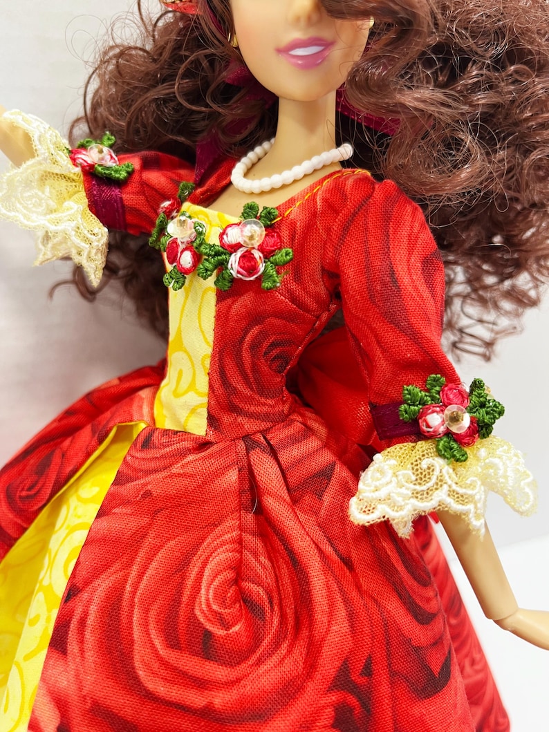 May include: A doll wearing a red dress with a rose pattern. The dress has yellow accents and is adorned with floral embellishments. The doll has brown hair and a pearl necklace. The sleeves have lace cuffs.