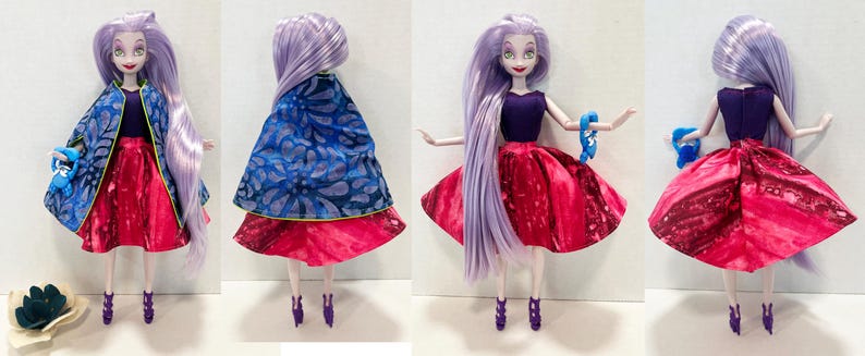 Pu&ograve; includere: Una bambola con lunghi capelli color lavanda indossa un top smanicato viola scuro, una gonna svasata rosa acceso e un mantello blu con un motivo floreale scuro. La bambola ha scarpe con tacco viola e tiene in mano un piccolo accessorio blu.