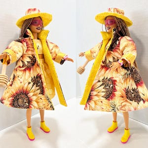 Puede incluir: Dos mu&ntilde;ecas vestidas con trajes con tem&aacute;tica de girasoles. Cada mu&ntilde;eca lleva un sombrero amarillo, gafas de sol rosas y un abrigo largo con estampado de girasoles. Tambi&eacute;n tienen botas amarillas con suelas rosas y sostienen un cuchar&oacute;n de miel de madera.