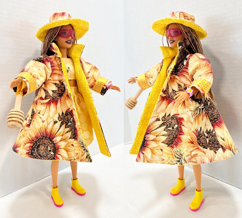Puede incluir: Dos mu&ntilde;ecas vestidas con trajes con tem&aacute;tica de girasoles. Cada mu&ntilde;eca lleva un sombrero amarillo, gafas de sol rosas y un abrigo largo con estampado de girasoles. Tambi&eacute;n tienen botas amarillas con suelas rosas y sostienen un cuchar&oacute;n de miel de madera.