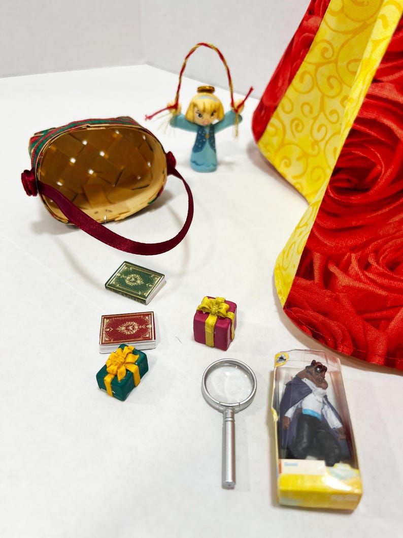 May include: A collection of miniature decorative items, including a woven basket with a burgundy handle, small gift boxes with yellow bows, and a magnifying glass. Also present are two miniature books, a figurine of a girl, and a figurine of a character in a clear plastic case.