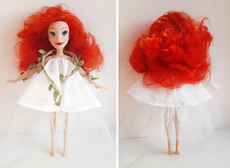 Puede incluir: Una mu&ntilde;eca de pelo rojo con un vestido blanco con un detalle de vid verde y una falda de tul blanca.