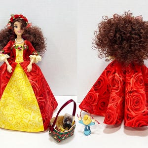 May include: A doll in a red rose-patterned gown with a yellow panel, a floral crown, and a pearl necklace. Accessories include a basket and small figurines. The doll's hair is styled in voluminous brown curls.