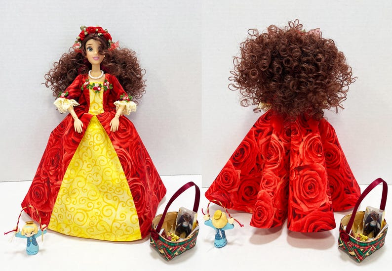 May include: A doll in a red rose-patterned gown with a yellow panel, a floral crown, and a pearl necklace. Accessories include a basket and small figurines. The doll's hair is styled in voluminous brown curls.