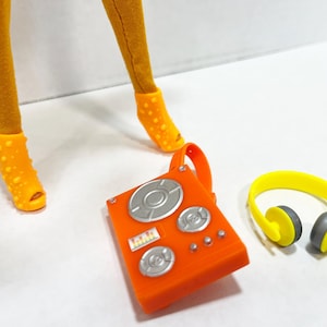 K&ouml;nnte beinhalten: Ein Paar senfgelbe Leggings, orangefarbene, genoppte Peeptoe-Schuhe, ein orangefarbenes DJ-Mischpult aus Kunststoff mit silbernen runden Drehreglern und einem kleinen rechteckigen Display sowie ein leuchtend gelber Kopfh&ouml;rer mit grauen Ohrpolstern.