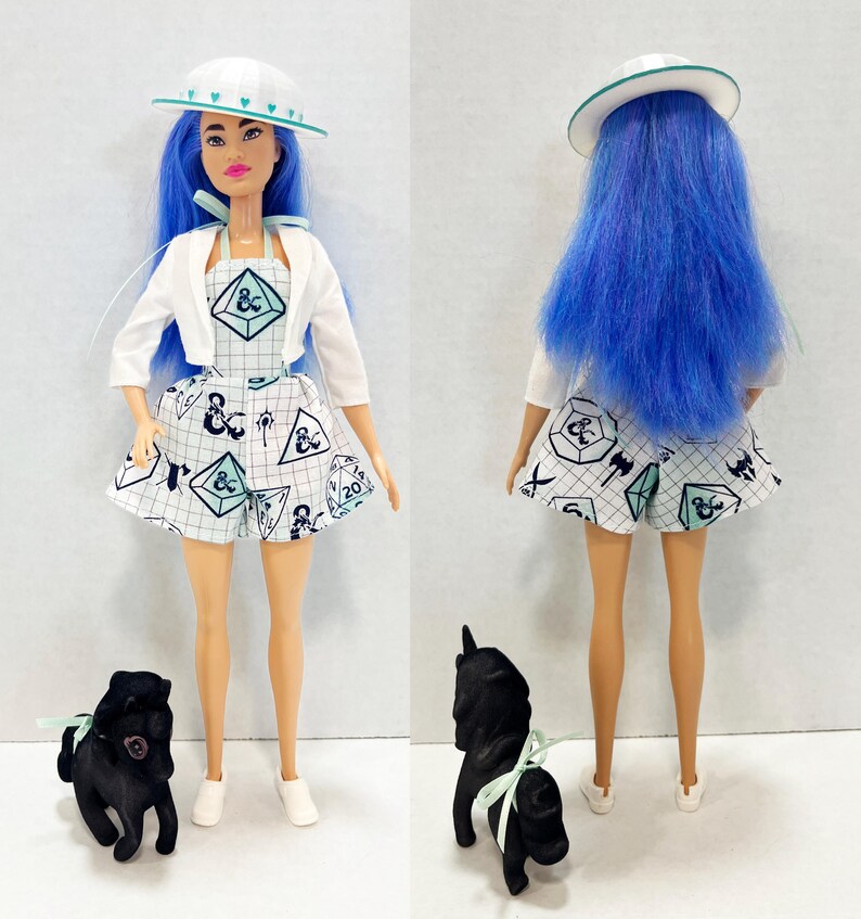 May include: A doll with long blue hair wearing a white hat with teal hearts, a white cropped jacket, and a white romper featuring a grid pattern with Dungeons and Dragons symbols. A small black dog figurine with a teal ribbon is positioned nearby.