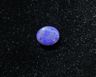 May include: A blue and white opal gemstone with a smooth, oval shape. The gemstone is set against a black background.