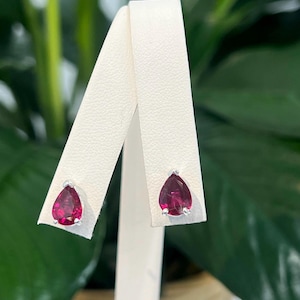 May include: A pair of silver stud earrings with pear-shaped red gemstones.