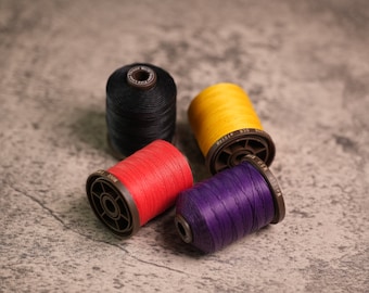 May include: Four spools of thread in black, red, yellow, and purple. The spools are made of plastic and have a metal cap.
