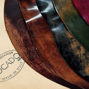 May include: Close-up of five different leather swatches, each a different color and texture. The swatches are arranged in a semi-circle, with the darkest swatch at the bottom and the lightest swatch at the top. The swatches are labeled "Shell Cordovan" and "Rocado" with the text "Made in Italy 1988".