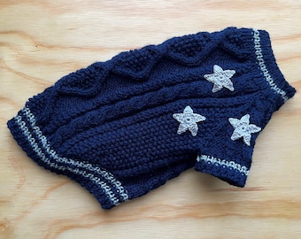 May include: A navy blue knitted dog sweater with white star embellishments. The sweater has a cable knit pattern and white trim around the edges.
