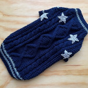 K&ouml;nnte beinhalten: Ein dunkelblauer gestrickter Hundepullover mit Zopfmuster und wei&szlig;en Stern-Applikationen.
