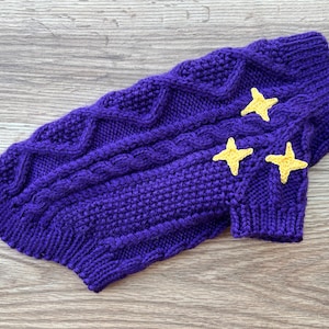K&ouml;nnte beinhalten: Lilafarbener Strickpullover f&uuml;r Hunde mit gelben Stern-Applikationen.