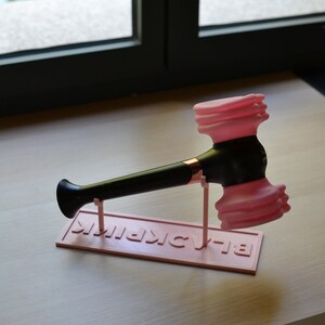 May include: A pink and black light stick with a hammer-shaped head and the word "BLACKPINK" printed on the base.