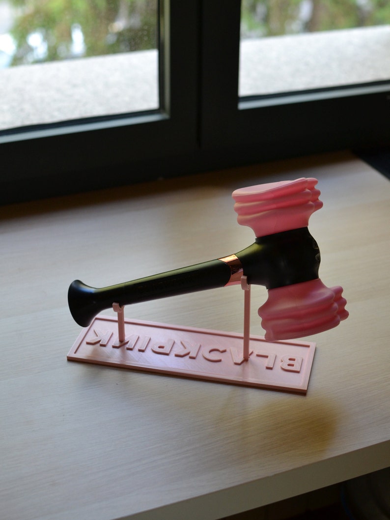 May include: A pink and black light stick with a hammer-shaped head and the word "BLACKPINK" printed on the base.