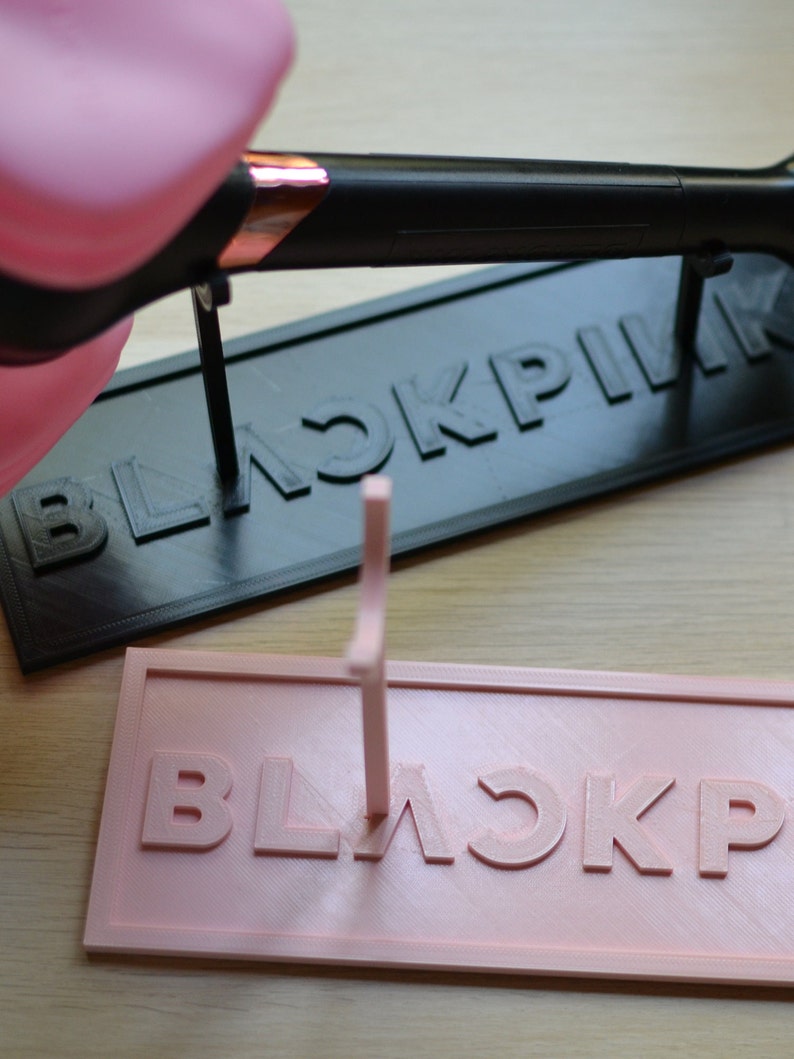 May include: A pink and black 3D printed stand with the word "BLACKPINK" printed on it. The stand is designed to hold a microphone.