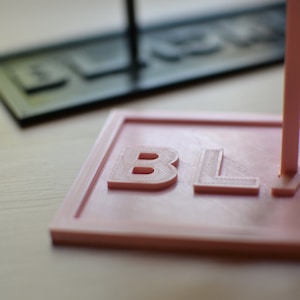 May include: A close-up of a pink 3D printed sign with the word "BLACK" embossed on it.