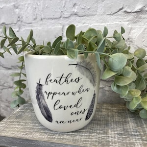 May include: White ceramic planter with a black and white feather design and the text "feathers appear when loved ones are near".