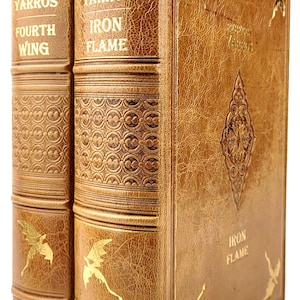 Op de afbeelding: Twee in leer gebonden boeken met gouden accenten en gegraveerde drakenontwerpen. De titels zijn "Rebecca Yarros Fourth Wing" en "Rebecca Yarros Iron Flame".