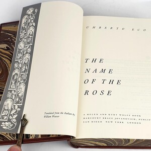 K&ouml;nnte beinhalten: Ein Buch mit dem Titel "Der Name der Rose" von Umberto Eco. Der Buchumschlag ist wei&szlig; mit schwarzem Text und einem marmorierten Design an den R&auml;ndern.
