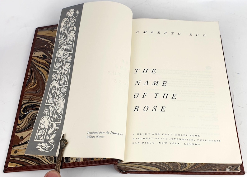K&ouml;nnte beinhalten: Ein Buch mit dem Titel "Der Name der Rose" von Umberto Eco. Der Buchumschlag ist wei&szlig; mit schwarzem Text und einem marmorierten Design an den R&auml;ndern.