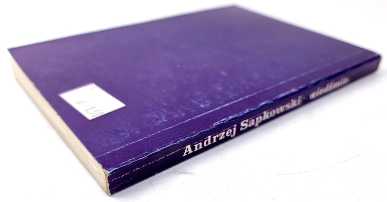 K&ouml;nnte beinhalten: Ein Hardcover-Buch mit lila Einband. Der Name des Autors, Andrzej Sapkowski, ist in Wei&szlig; gedruckt. Auf dem Einband befindet sich ein wei&szlig;es Etikett. Die Seiten sind cremefarben.