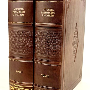 Op de afbeelding: Twee antieke bruin lederen boeken met gouden details. De ruggen tonen de titel "MITCHELL PRZEMINĘŁO Z WIATREM" in gouden letters, met "TOM I" en "TOM II" eronder. Gouden patronen sieren de boven- en onderranden.