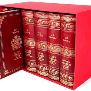 May include: A set of seven red leather-bound books with gold accents and titles. The books are titled "Harry Potter and the Philosopher's Stone", "Harry Potter and the Chamber of Secrets", "Harry Potter and the Prisoner of Azkaban", "Harry Potter and the Goblet of Fire", "Harry Potter and the Order of the Phoenix", "Harry Potter and the Half-Blood Prince", and "Harry Potter and the Deathly Hallows".