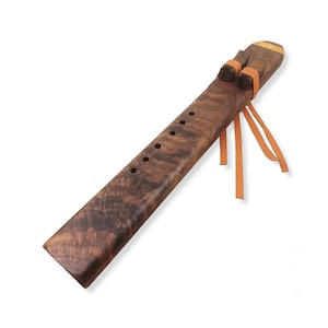 Könnte beinhalten: Eine Holzflöte mit dunkelbrauner Oberfläche und einem natürlichen Holzmaserungsmuster. Sie hat fünf Fingerlöcher und ist mit einem Lederriemen und Quasten verziert.