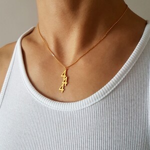 May include: A gold necklace with a pendant featuring the number 4 repeated three times.