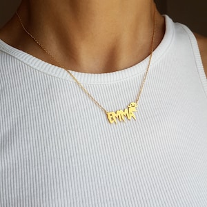 May include: A gold chain necklace with a nameplate pendant that says "EMMA" in a dripping font style.