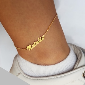 May include: Gold ankle bracelet with the name "Natalie" written in cursive.