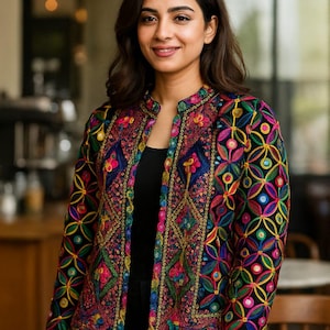 May include: A colorful, embroidered jacket with a black base. The jacket features intricate floral and geometric patterns in shades of pink, blue, yellow, and green. The jacket has a mandarin collar and long sleeves. The jacket is worn over a black top.