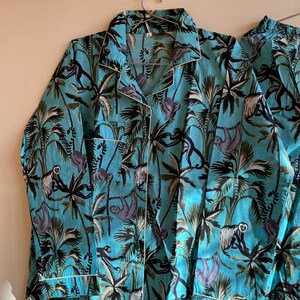 May include: A turquoise blue pajama top and pants set with a tropical print featuring sloths and palm trees. The fabric has a white trim.