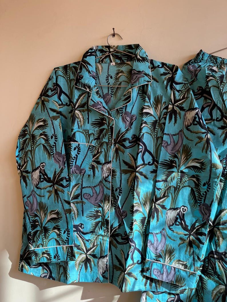 May include: A turquoise blue pajama top and pants set with a tropical print featuring sloths and palm trees. The fabric has a white trim.