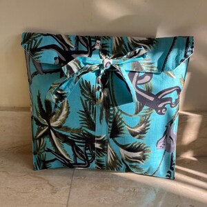 May include: A turquoise blue fabric gift bag with a tropical print of palm trees and monkeys. The bag has a fabric tie closure.