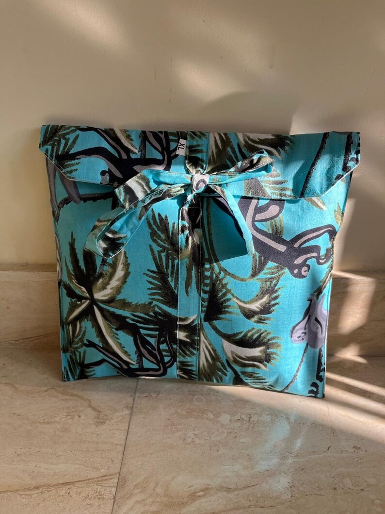 May include: A turquoise blue fabric gift bag with a tropical print of palm trees and monkeys. The bag has a fabric tie closure.