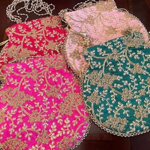 May include: Four embroidered drawstring pouches in red, pink, rose, and teal. Each pouch has gold floral embroidery and a beaded trim. The pouches are displayed on a dark wooden surface. The pouches are likely for carrying small items.