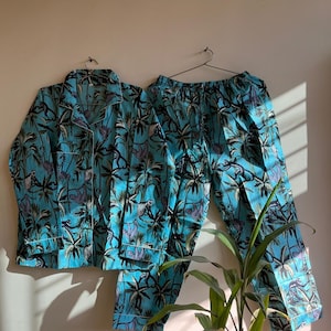 May include: A turquoise blue pajama set with a tropical print featuring palm trees and monkeys. The set includes a long-sleeved shirt with a button-up collar and matching pants.