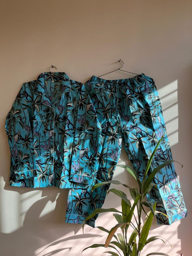 May include: A turquoise blue pajama set with a tropical print featuring palm trees and monkeys. The set includes a long-sleeved shirt with a button-up collar and matching pants.