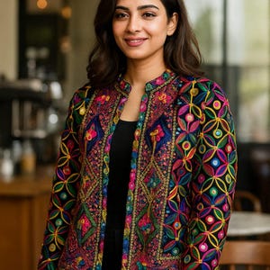 Puede incluir: Chaqueta bordada colorida con base negra. La chaqueta presenta intrincados patrones florales y geométricos en tonos rosa, azul, amarillo y verde. La chaqueta tiene cuello mandarín y está abierta por delante.