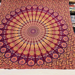 May include: A large, rectangular tapestry with a mandala design. The central pattern is a circular arrangement of stylized peacock feathers in shades of burgundy, orange, and yellow. The border features a repeating floral pattern in similar colors.